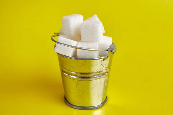 A small bucket with cubes of pressed sugar on a yellow background.