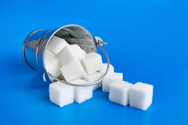 A small bucket with cubes of pressed sugar on a blue background.