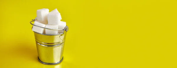 A small bucket with cubes of pressed sugar on a yellow background.