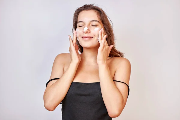 A girl applies foam on her face to clean her skin. Face care concept.