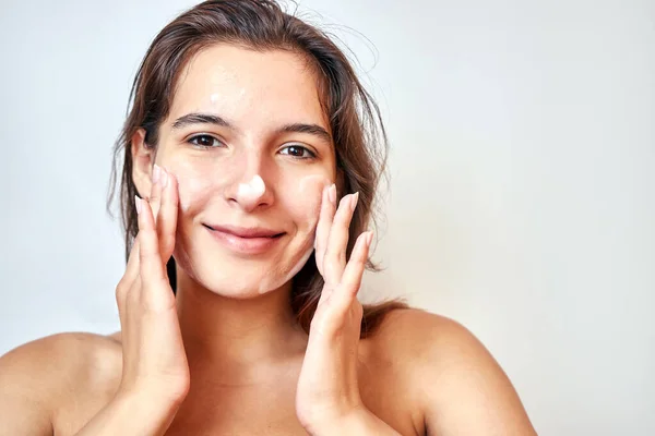 A girl applies foam on her face to clean her skin. Face care concept.