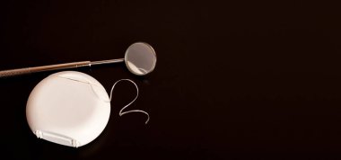 Dişçi aynası ve siyah arka planda diş ipi. Diş bakımı.