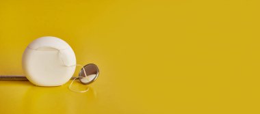 Dişçi aynası ve sarı arka planda diş ipi. Diş bakımı.