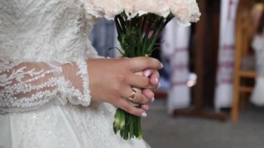 During the wedding ceremony, the bride holds a beautiful bouquet of white flowers in her hands.