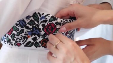 A friend helps the bride to put on her wedding dress by fastening the belt.