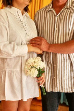 The bride, standing next to the groom, holds a bouquet of flowers in her hands.