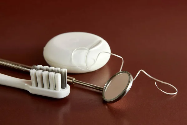 Dental mirror, dental floss and toothbrush on a brown background. Dental care.