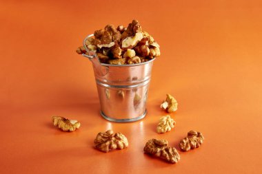 Turuncu arka planda ceviz dolu küçük metal bir kova. Sağlıklı beslenme kavramı.