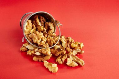 Kırmızı arka planda ceviz dolu küçük metal bir kova. Sağlıklı beslenme kavramı.