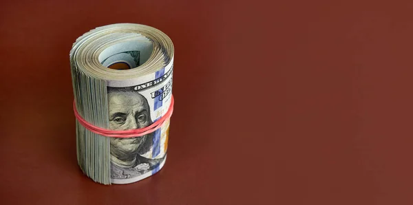 Many Hundred Dollar Bills Rolled Red Rubber Band Brown Background — стоковое фото