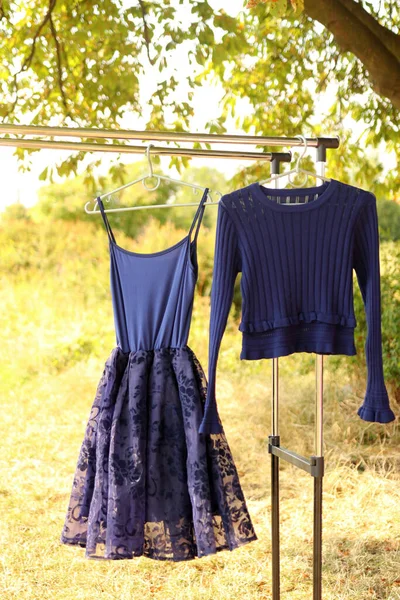 A blue dress and a sweater are hanging on a hanger.