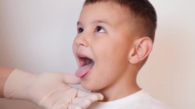 Doktor çocuğun boğazını incelemek için bir spatula kullanıyor..