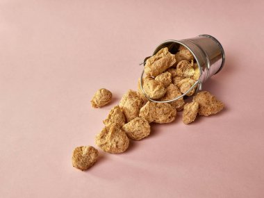 Pembe arka planda küçük bir kovada desenli soya unu parçaları..