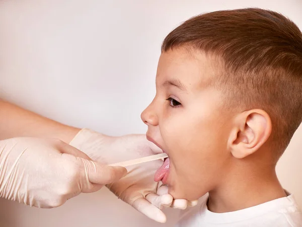 Doktor çocuğun boğazını incelemek için bir spatula kullanıyor..
