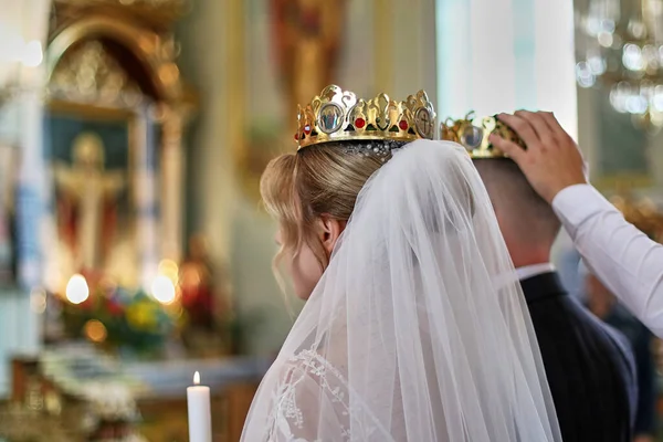 Grooms with crowns on their heads in the church during the wedding ceremony.