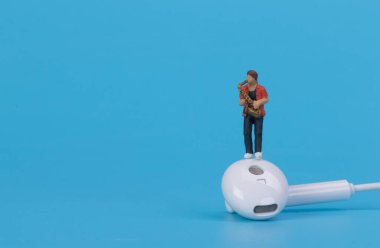 Mavi arka planda kulaklık takan minyatür müzisyen