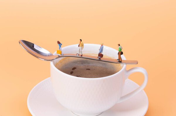 Miniature people walking on the spoon over the hot cup of coffee
