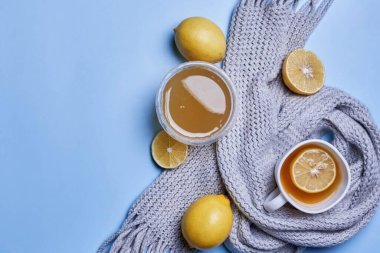 Bir fincan limonlu sıcak çay, bal ve mavi arka planda eşarp.