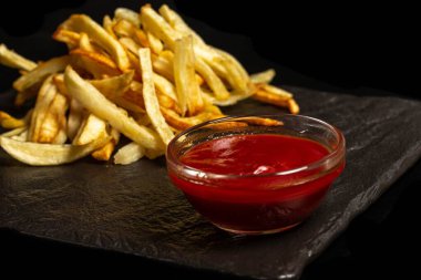 Siyah arka planda domates sosu ve kızarmış patates.