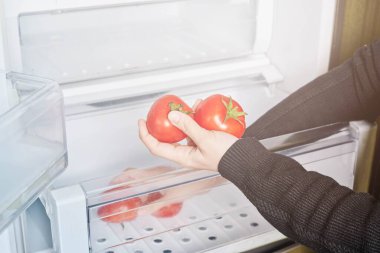Woman taking fresh tomatoes from the salad crisper drawers of re
