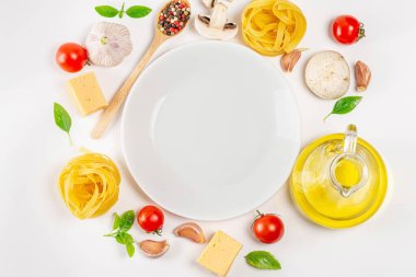 Top view of pasta, raw vegetables and spices on white background