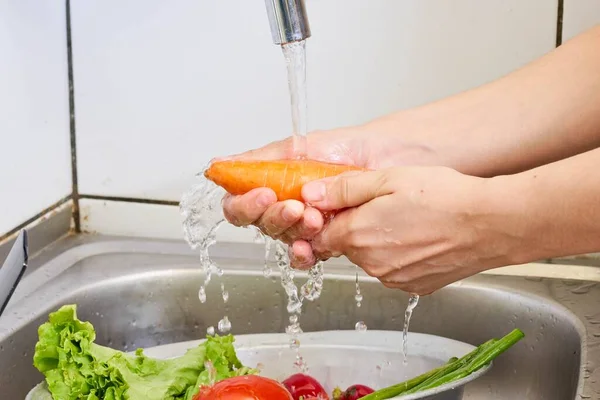 Carrots are washed under running water in a colander