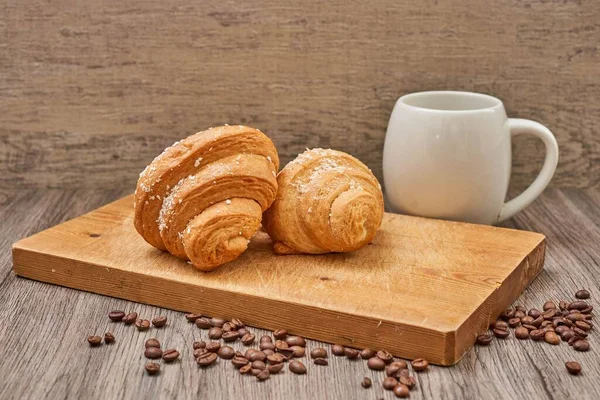Coffee cup and raw coffee beans with tasty croissants on the woo