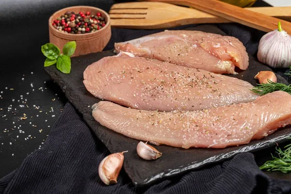 Koyu arkaplanda baharatlı çiğ tavuk filetosu.