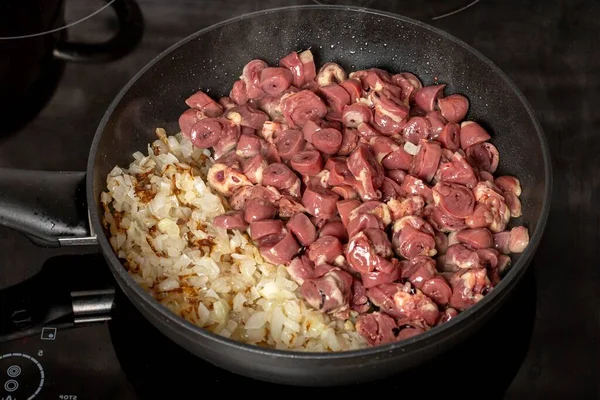 Pieces of hearts in a skillet with fried onions on the stove