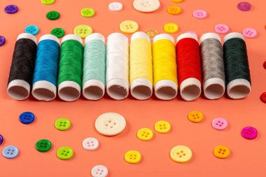 Multicolored threads and buttons on an orange background