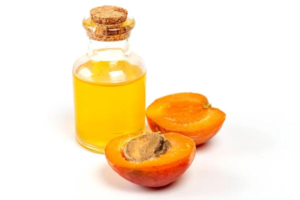 Halves of a ripe apricot and a bottle of oil on a white backgrou