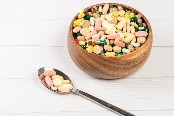 Wooden bowl with a spoon filled with medicine pills on a white w