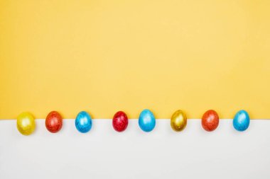 Sarı ve beyaz arka planda renkli Paskalya yumurtaları.