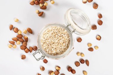 Üst manzara, beyaz üzerine yulaf ezmesi kavanozu, fındık ve badem.