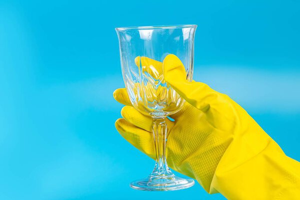 Female hand in a rubber glove holds a wine glass on a blue backg