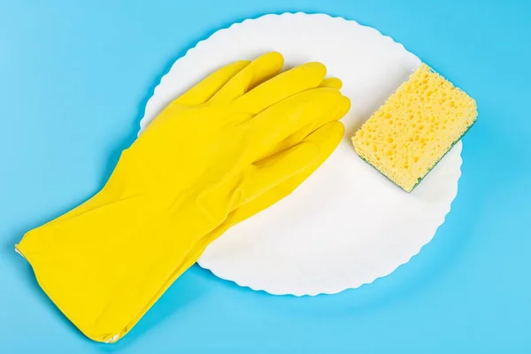 White plate, rubber gloves and a sponge on a blue background