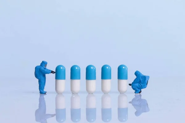 Miniature workers in safety uniforms with pills on light blue ba