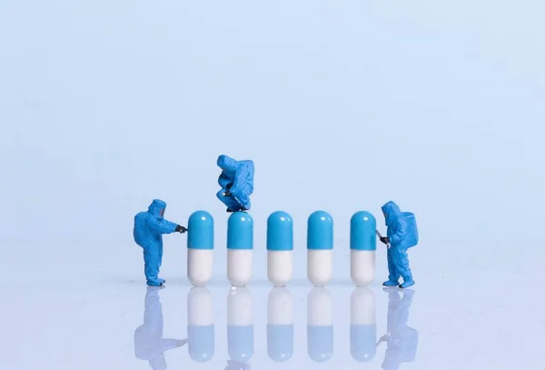 Miniature workers in safety uniforms and pills on light blue bac