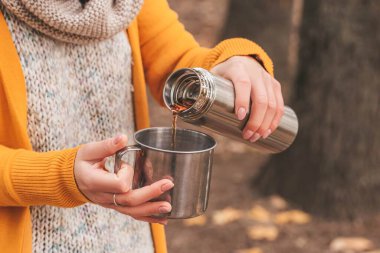 Hands of a girl pour tea from a thermos into a mug on an autumn 