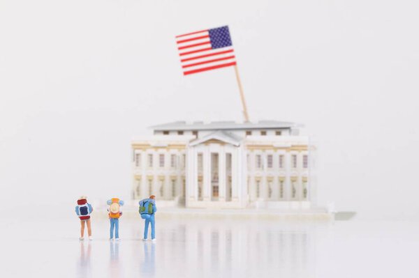 Miniature travelers stading in front of the White House on white
