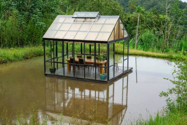 Tisch Stuhle in einem Glashaus in der Mitte eines Teiches 