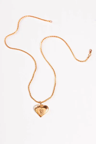 Gold chain and pendant in the shape of a heart on a white backgr