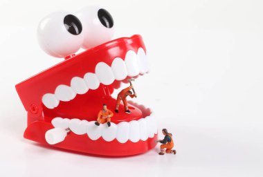 Miniature people cleaning teeth on white backgroudn