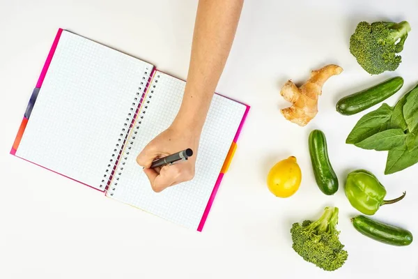 Woman writing on a notepad. Weight-loss planning with fresh vege