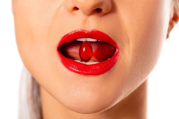 Close-up, a woman with an open mouth holds a red capsule in her