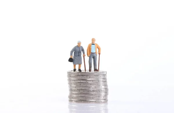 Old couple standing on top of stack of coins on white background