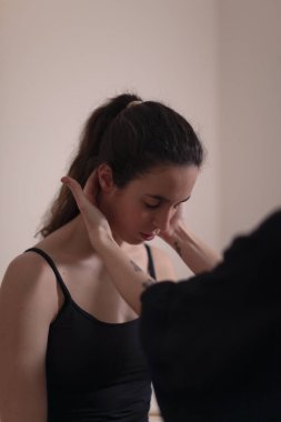Bir kadın terapist, sırt ağrısını dindirecek masaja başlamadan önce masaj masasında hastasının boynunu muayene eder.