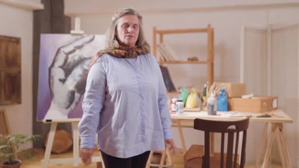 ผู้หญิงศิลปินผู้สูงอายุ มองกล้องในห้องทํางานของเธอ — วีดีโอสต็อก