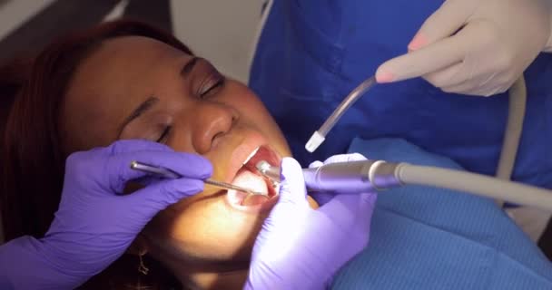 歯医者は歯のクリニックで歯肉炎を防ぐために歯茎や歯をチェックし きれいにしながら黒人女性患者は彼女の口を開いておく — ストック動画