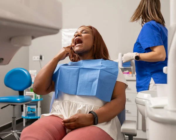 A black woman patient points with her index finger where the pain is developing, so the dentist know how to do the treatment at the dental clinic